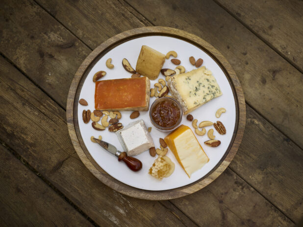 Cheese platter on a round wooden platter with various cheeses, nuts and honeycomb on a rustic wooden background