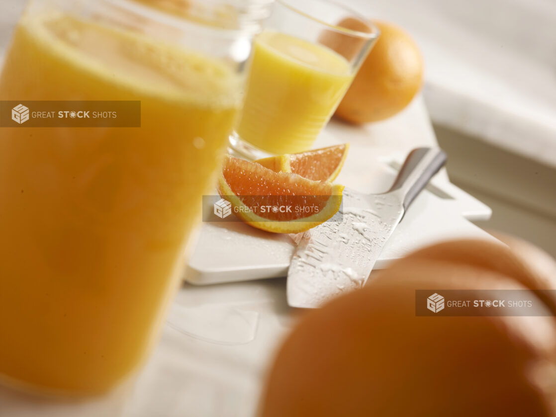 Freshly squeezed orange juice with whole and sliced oranges and oranges sliced on a white cutting board with a knife