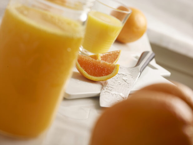 Freshly squeezed orange juice with whole and sliced oranges and oranges sliced on a white cutting board with a knife