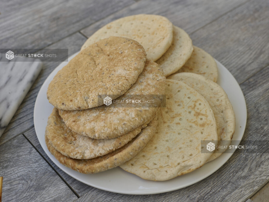 Multigrain and white mini pitas on a white round plate in a close up view on a grey wooden background