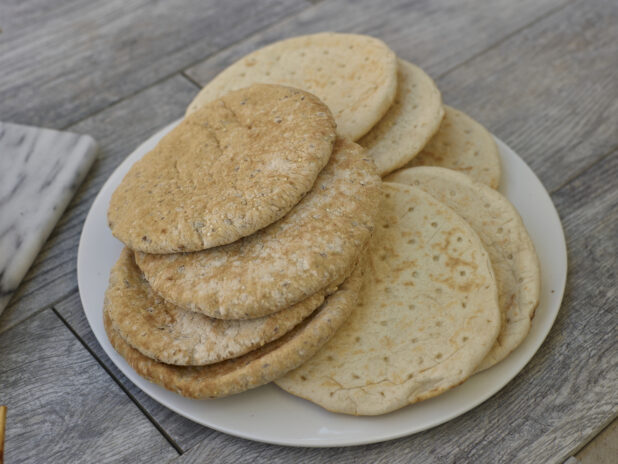 Multigrain and white mini pitas on a white round plate in a close up view on a grey wooden background