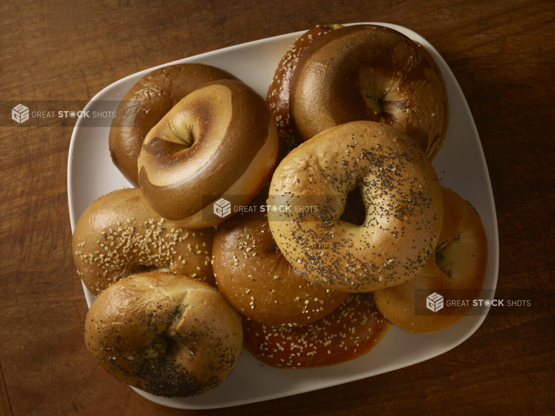 Assorted bagels on a rounded square plated on a rustic wooden background