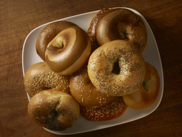 Assorted bagels on a rounded square plated on a rustic wooden background