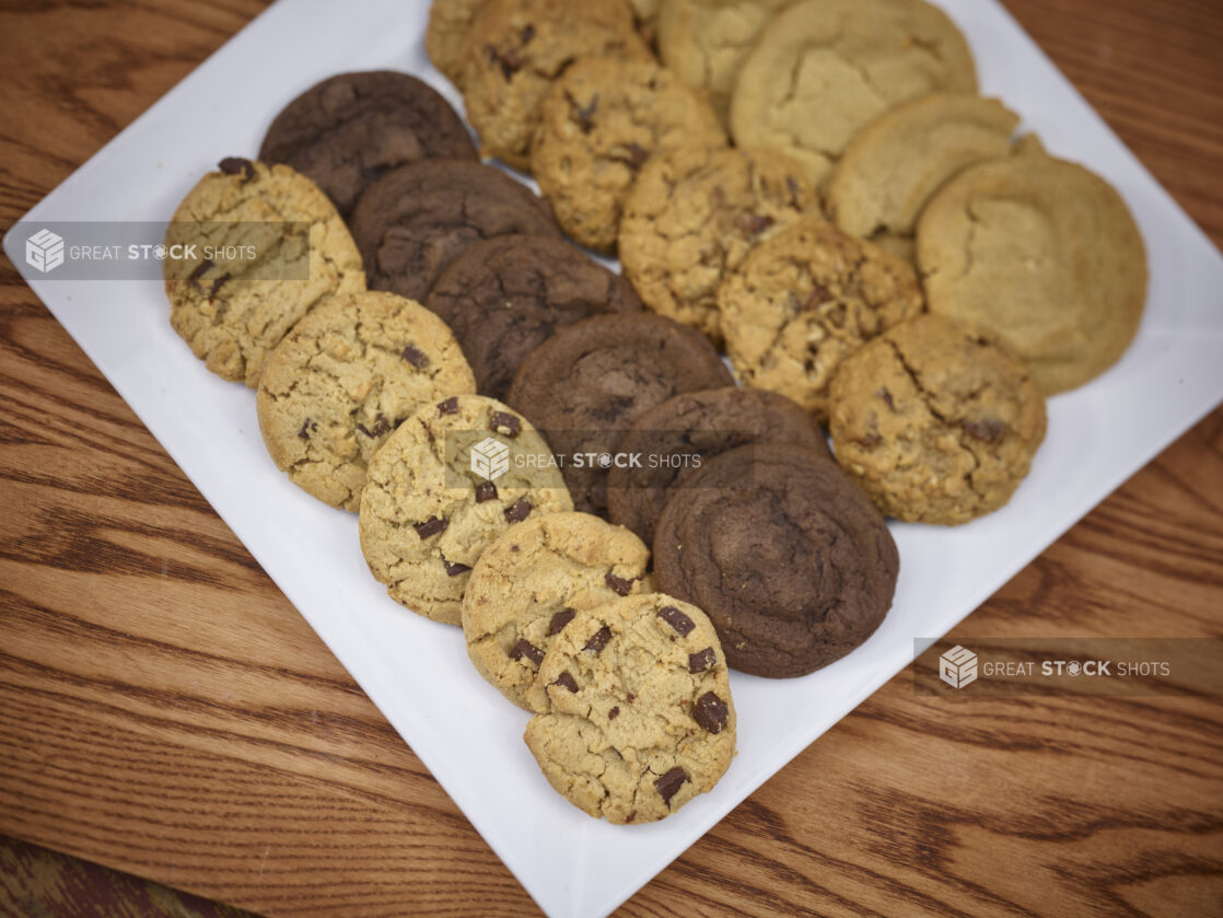 Assorted cookies, chocolate chips, double chocolate, oatmeal raisin and peanut butter on a square white platter on a wooden background