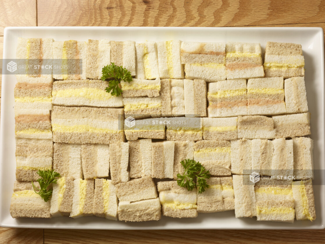 Overhead view of party/finger sandwiches of tuna salad, egg salad and salmon salad on a rectangular white platter