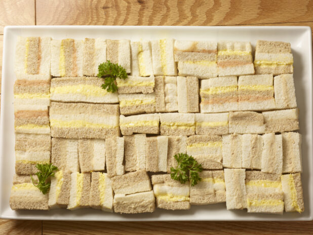 Overhead view of party/finger sandwiches of tuna salad, egg salad and salmon salad on a rectangular white platter