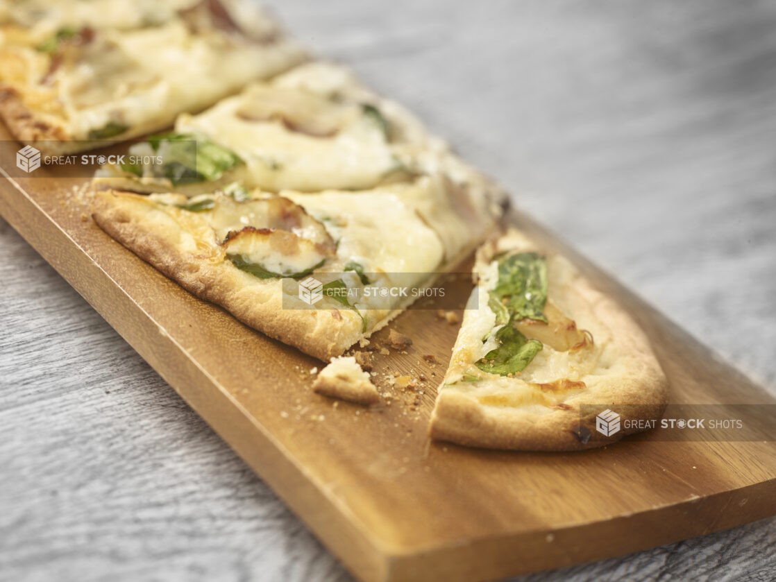 Sliced flatbread with bacon, arugula and cheese on a wooden board on a grey wooden background