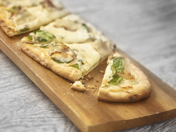 Sliced flatbread with bacon, arugula and cheese on a wooden board on a grey wooden background