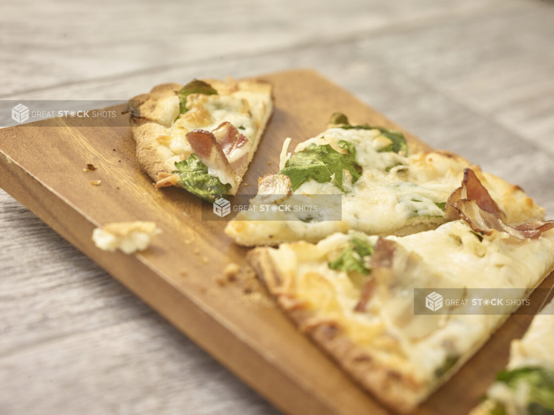 Cut flatbread with arugula, bacon and cheese in a close up view on a wooden board on a grey wooden background