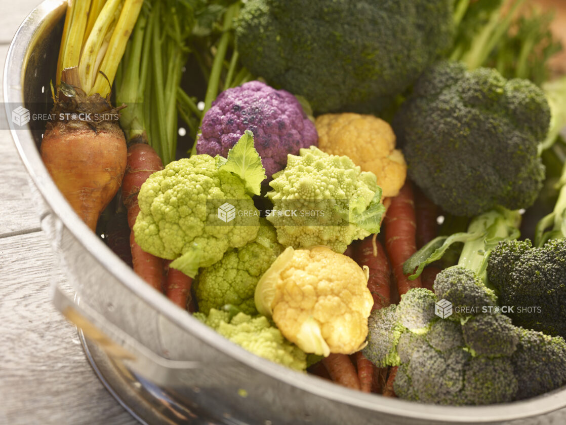 Fresh assorted heirloom and regular  vegetables in a silver colander, close up view, with a grey wooden background