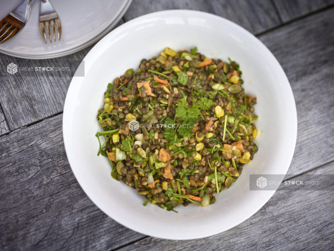 Lentil salad with corn, carrots, sweet potato, parsley, in a round white bowl on a grey wooden background