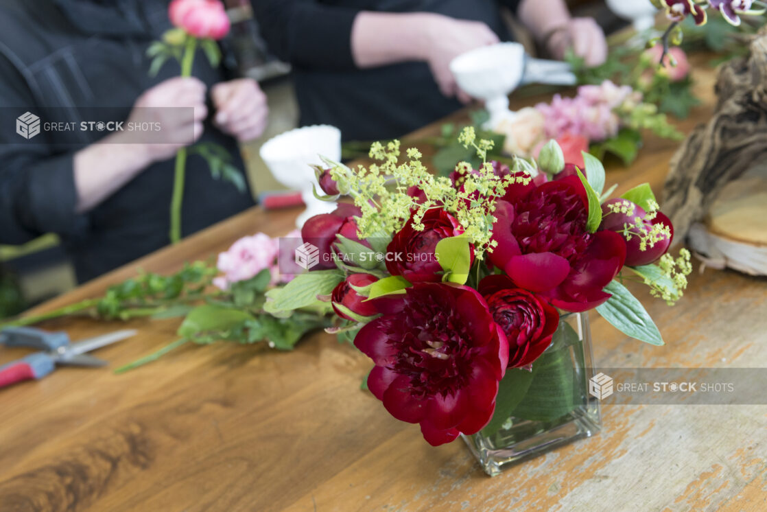 Flower arrangement in the foreground, 2 people and flowers in the background