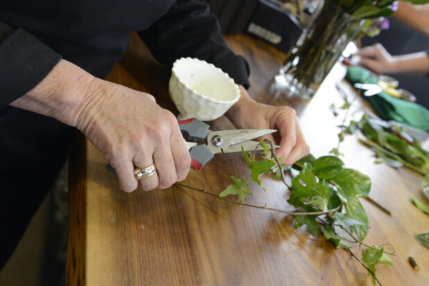 A pair of hands cutting a piece of ivy for a floral arrangement in a floral shop setting