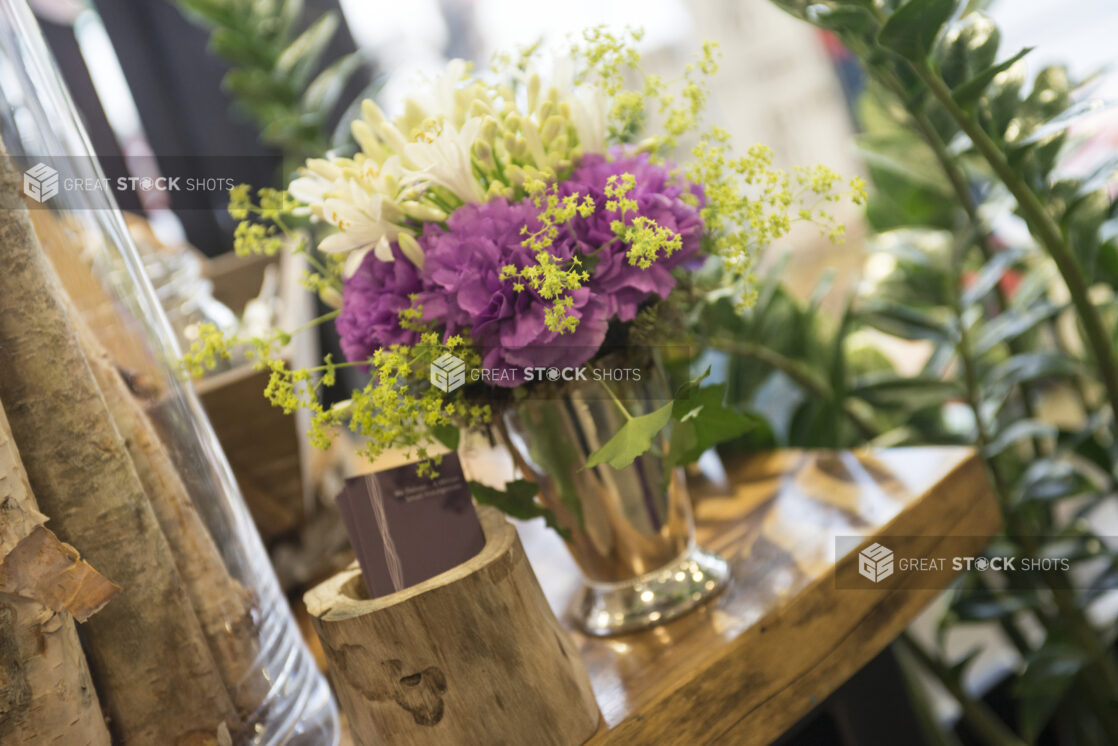 Floral arrangement with white freesia and purple carnations in a silver vase in a flower shop setting