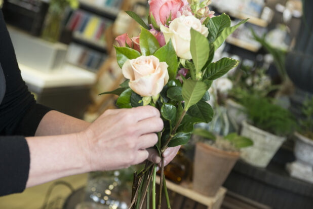 Hands making a flower arrangement with roses in a florist shop