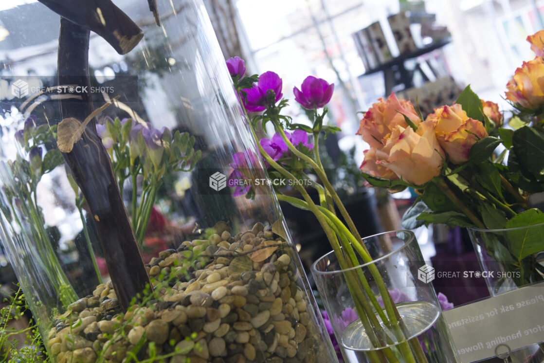 View of florist shop with clear glass vases up close with roses, vibrant flowers and pebbles