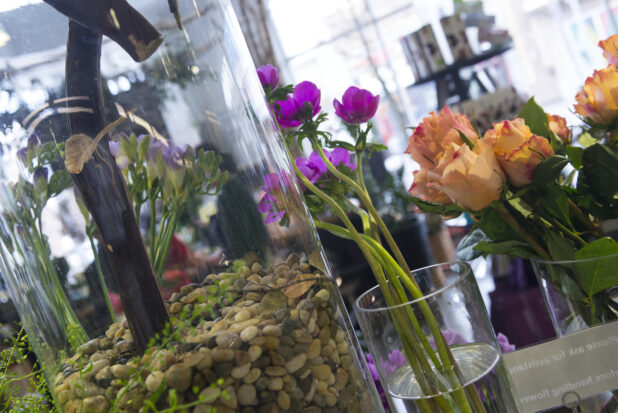 View of florist shop with clear glass vases up close with roses, vibrant flowers and pebbles