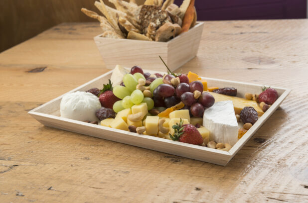 Assorted fruit and cheese platter on a wood catering tray with breadsticks in the background