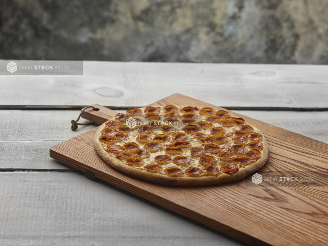 Whole pepperoni pizza on a wooden board on a grey wooden background