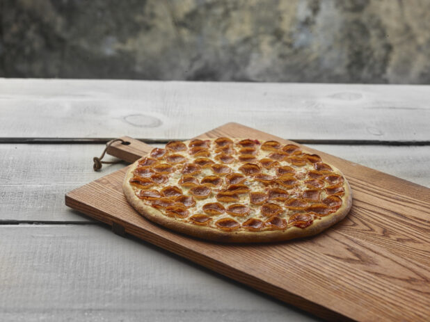 Whole pepperoni pizza on a wooden board on a grey wooden background