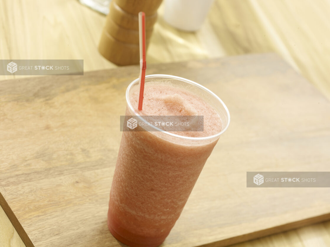 Fruit smoothie in a clear plastic on a wooden board with a wooden background