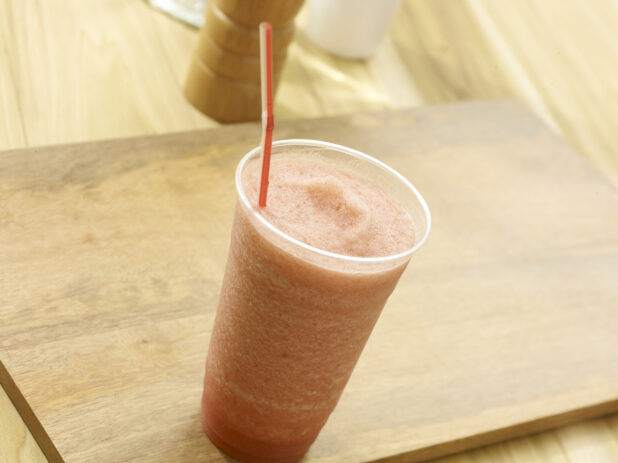Fruit smoothie in a clear plastic on a wooden board with a wooden background