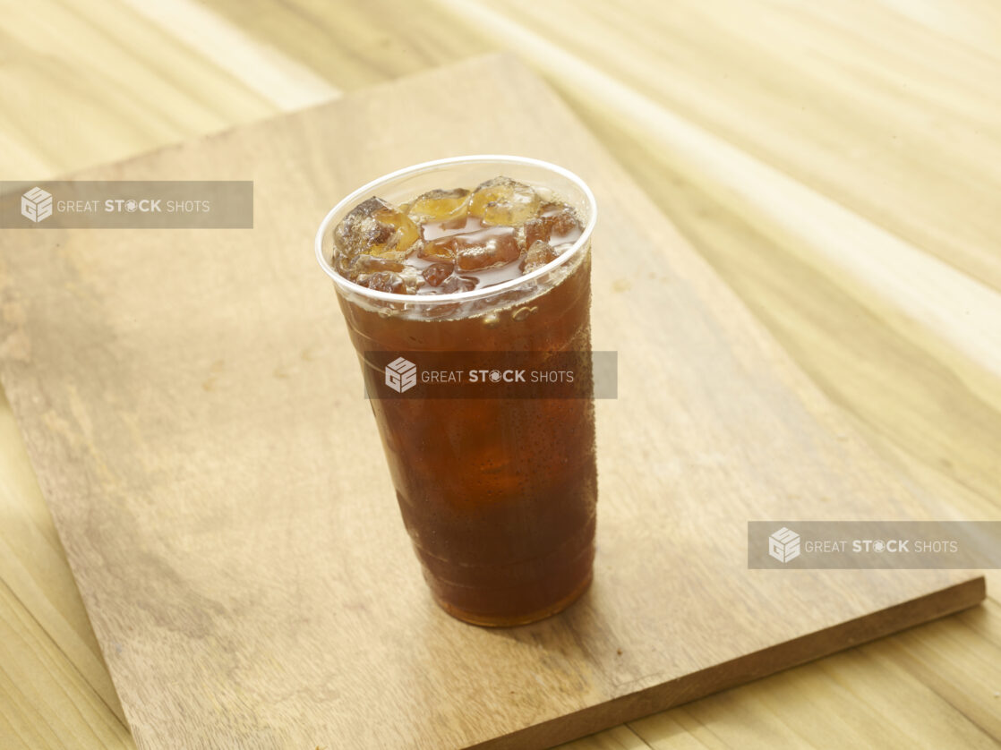 Iced tea in a clear plastic cup on a wooden board on a wooden background