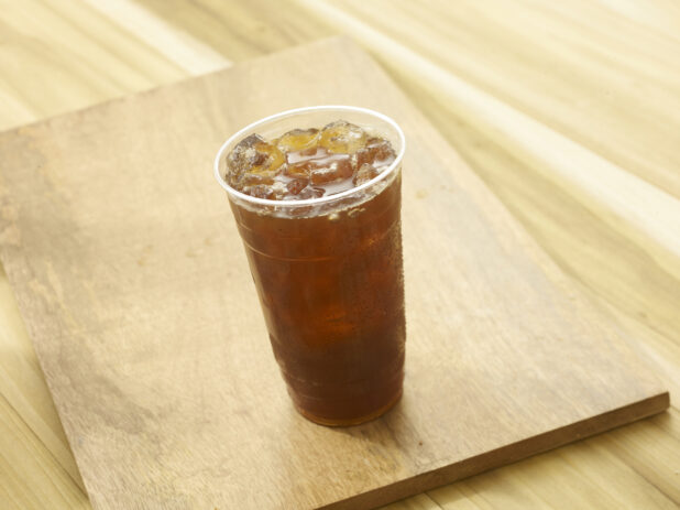 Iced tea in a clear plastic cup on a wooden board on a wooden background
