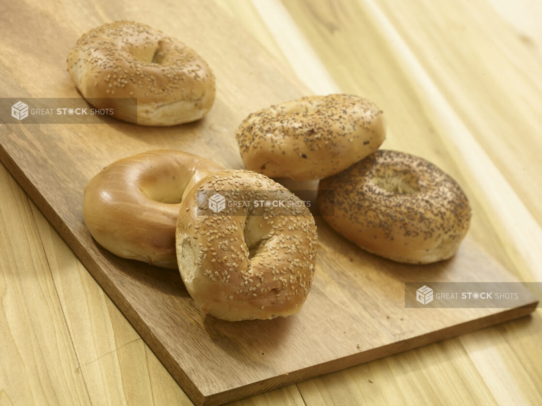 Assorted whole bagels on a wooden board and a wooden background