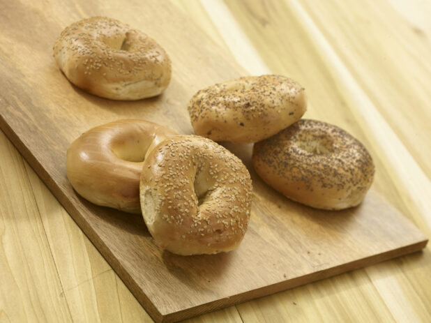 Assorted whole bagels on a wooden board and a wooden background