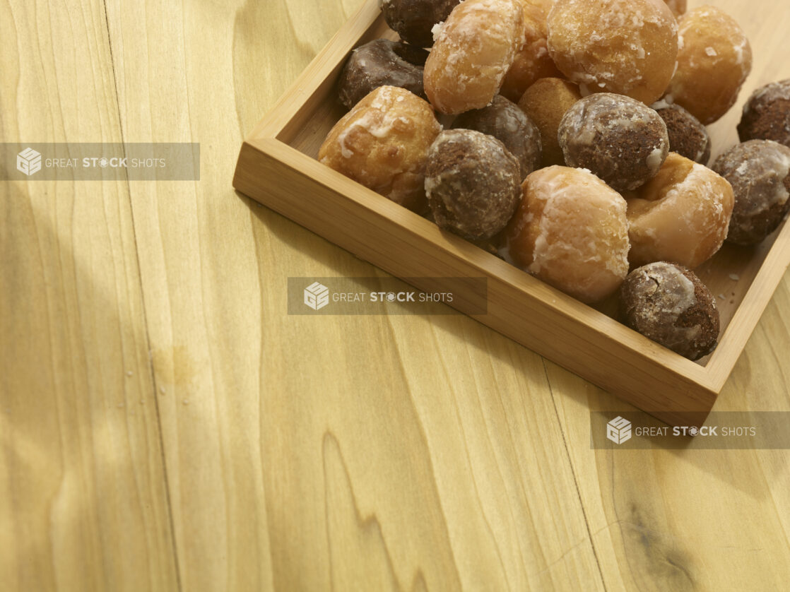 Assorted donut holes in a wooden box on a wooden background