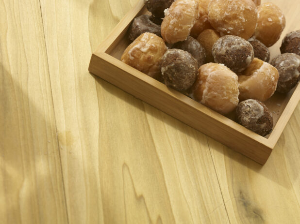 Assorted donut holes in a wooden box on a wooden background