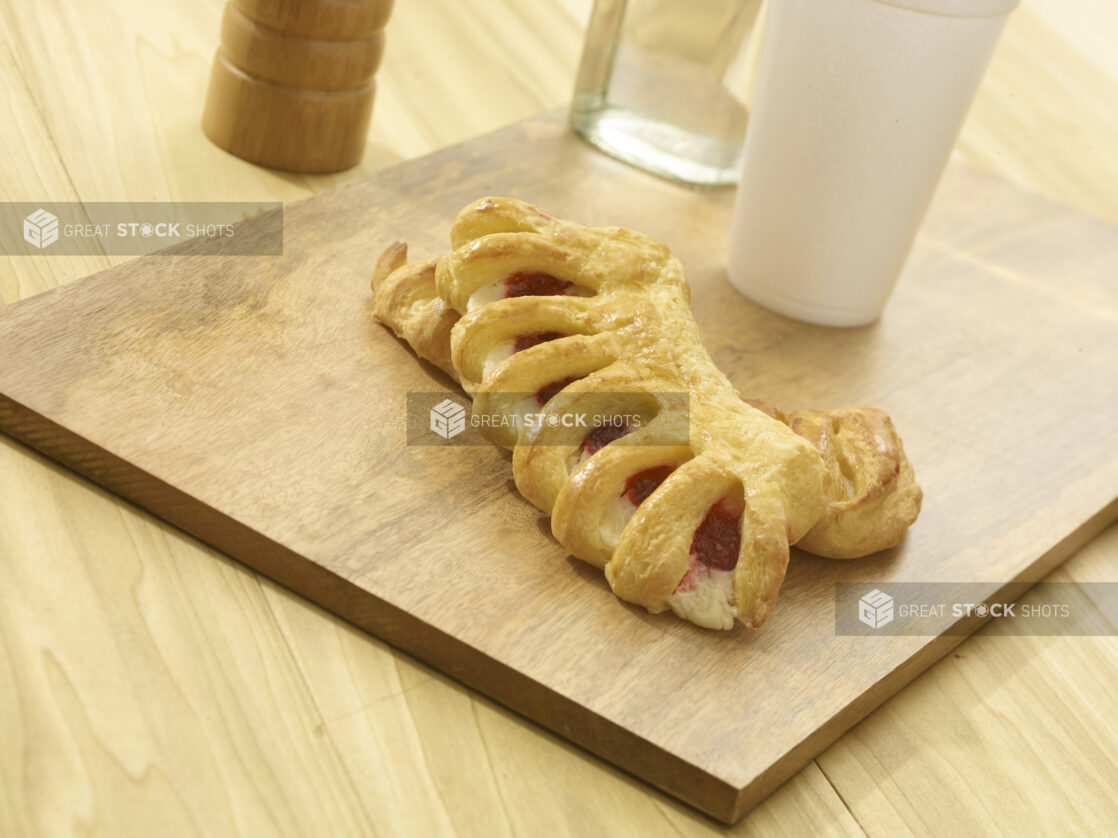 Whole raspberry turnover on a wooden board with accessories in the background