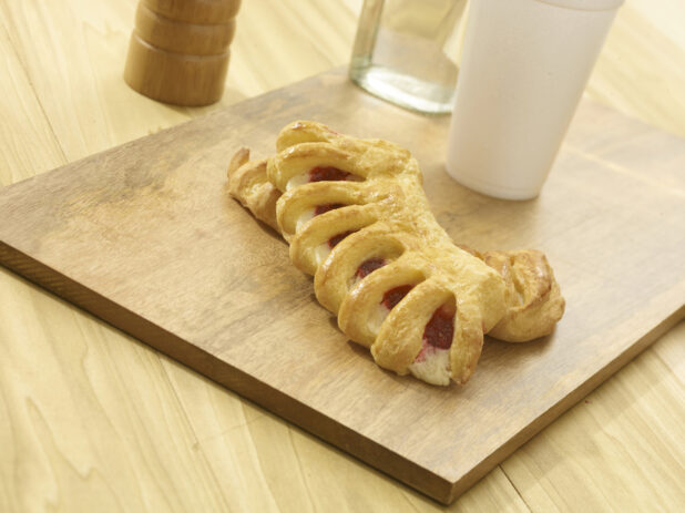 Whole raspberry turnover on a wooden board with accessories in the background