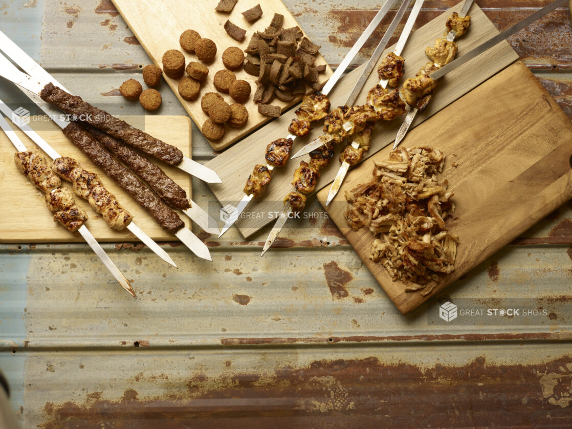 Middle Eastern meats and chicken on skewers, sliced chicken shawarma, falafel and gyros all displayed on wooden boards on a rustic tin background