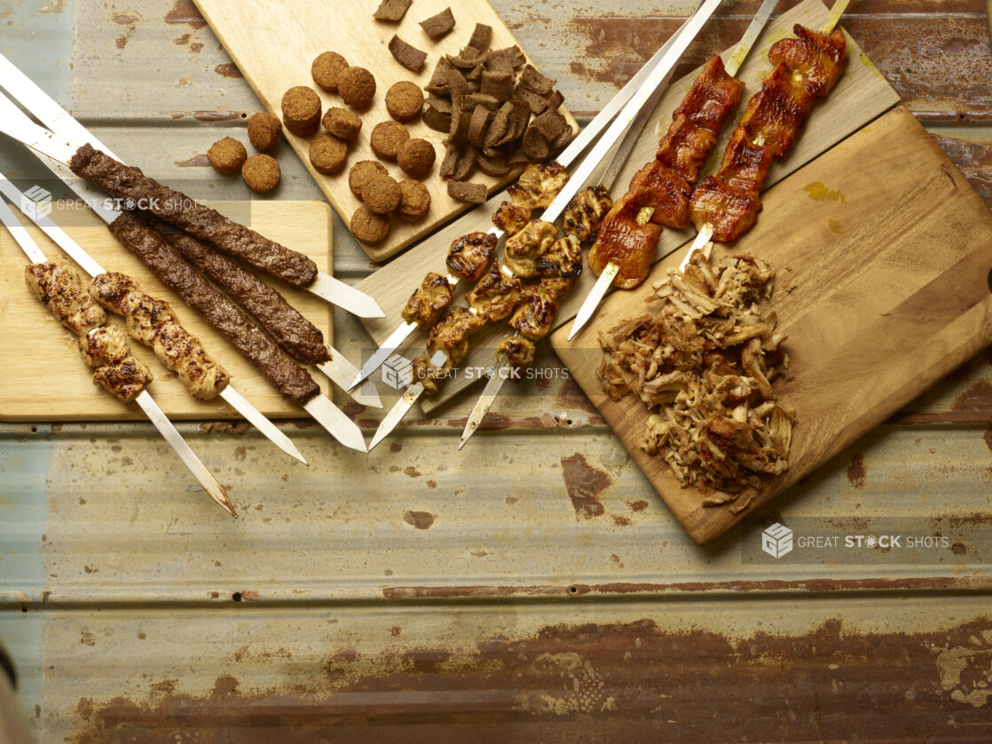 Middle Eastern meats and chicken on skewers, sliced chicken shawarma, falafel and gyros all displayed on wooden boards on a rustic tin background