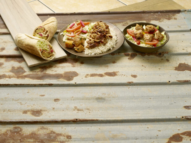 Chicken shawarma dinner, falafel wrap and a chicken kabob salad on a rustic tin background