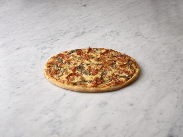 Whole salami and mushroom pizza on a white marble background