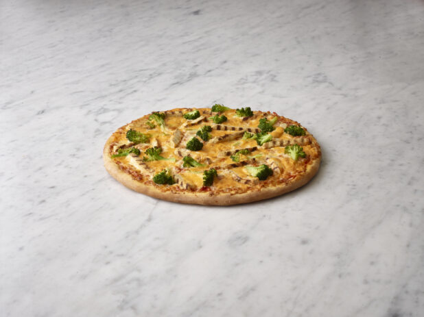 Whole chicken and broccoli pizza on a white marble background