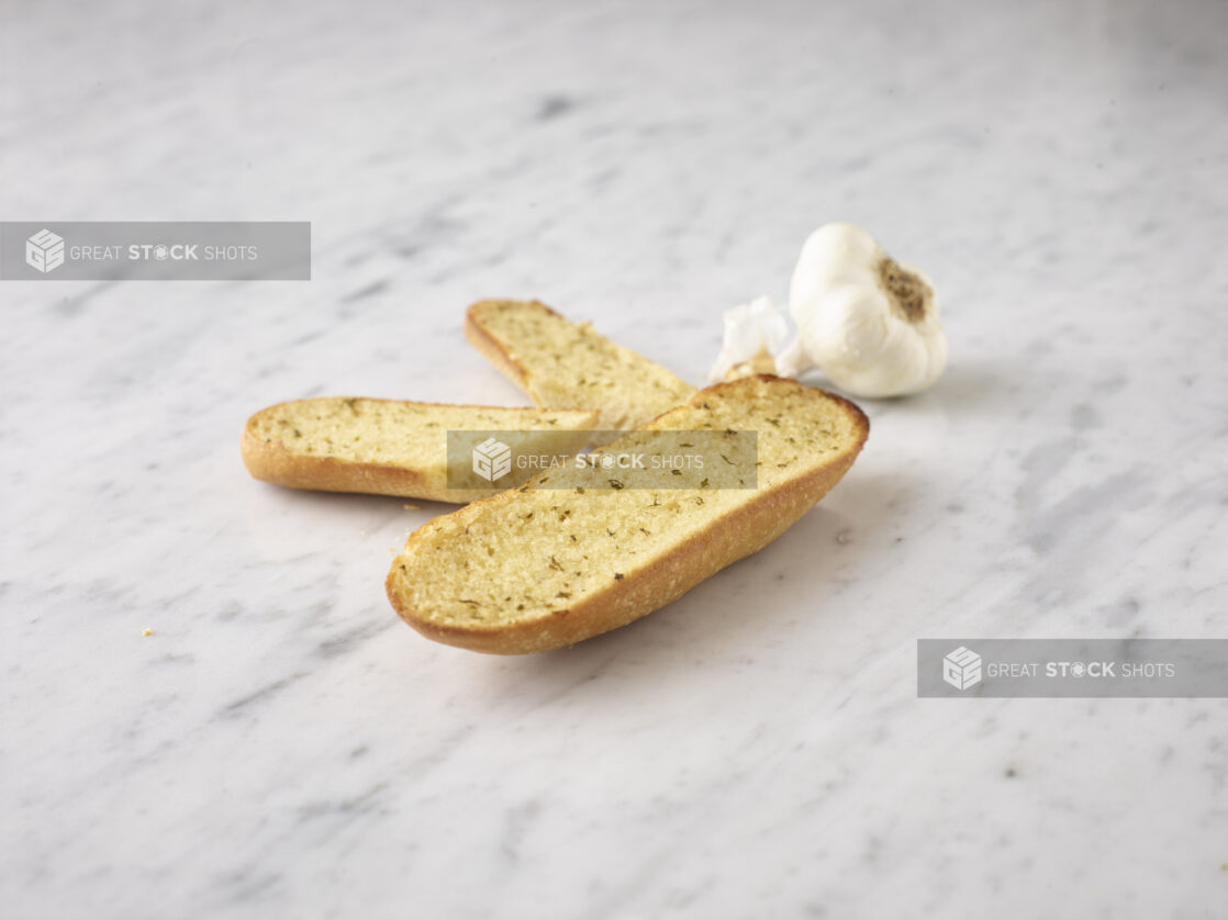 Garlic bread with a whole fresh garlic bulb all on a white marble background