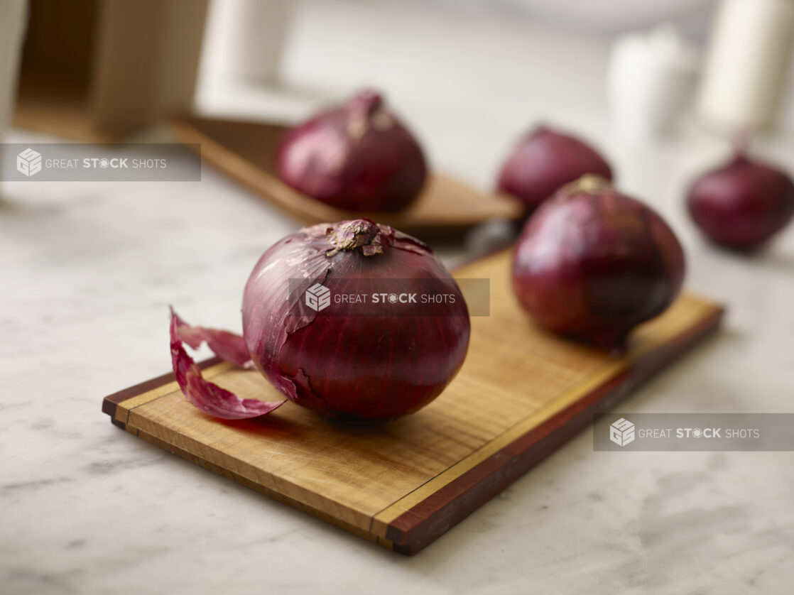 Whole red onions in the foreground and background on rustic wooden planks on a white marble background