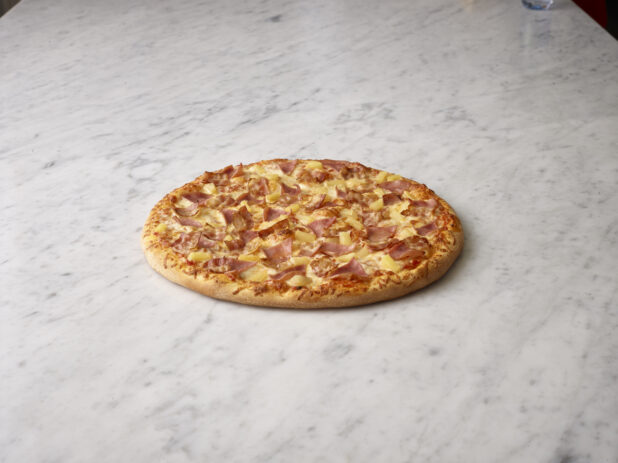 Whole Hawaiian pizza on a white marble background