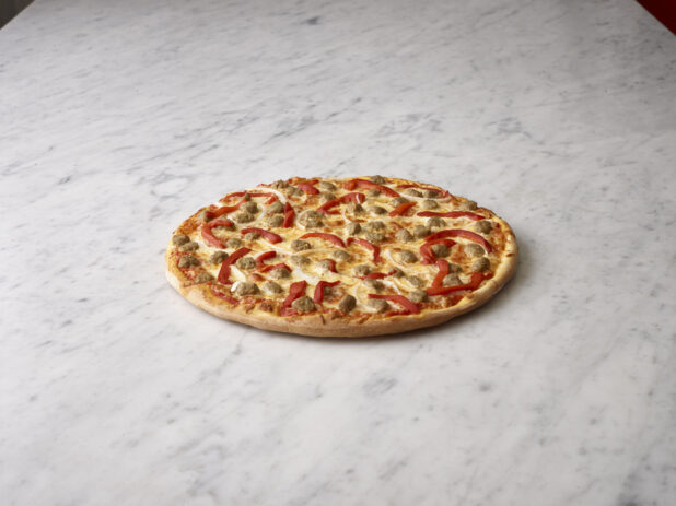 Whole sausage, roasted red pepper and onion pizza on a white marble background