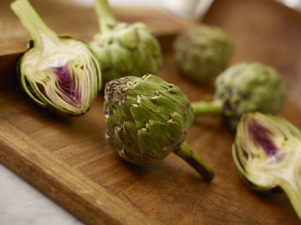 Fresh whole and sliced artichoke on a wooden board on a 45 degree angle