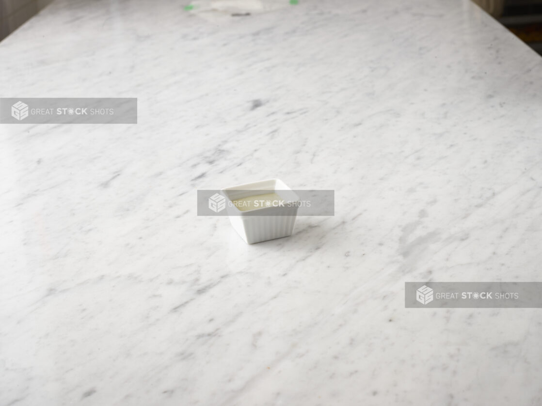 Grated parmesan cheese in a white ramekin on a white marble background