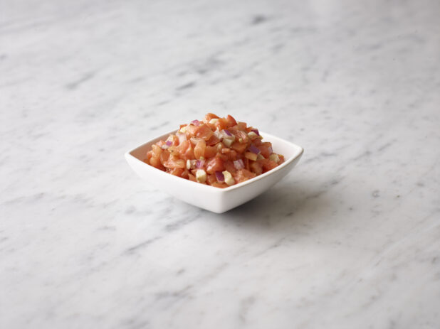 Bruschetta mix in a white square bowl on a white marble background