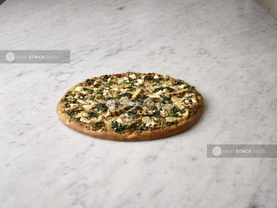 Whole 3 topping pizza with chicken, feta cheese and spinach, on a white marble background