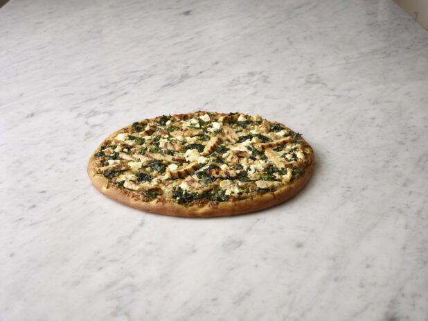 Whole 3 topping pizza with chicken, feta cheese and spinach, on a white marble background