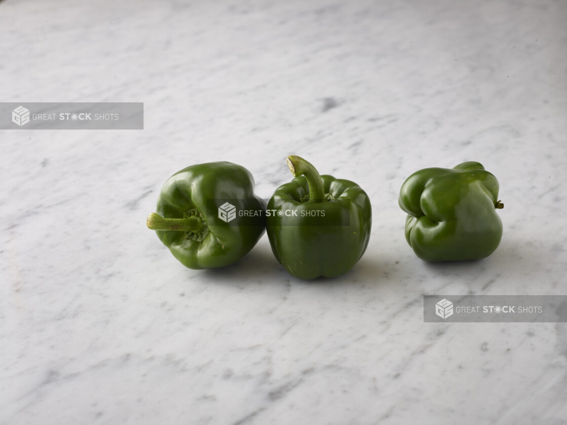 Three whole green bell peppers on a white marble background