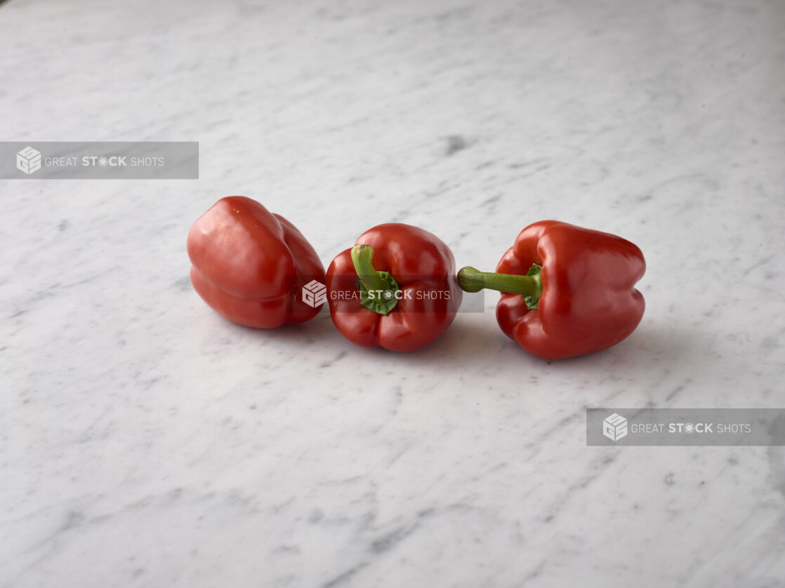 Whole fresh red bell peppers on a white marble background